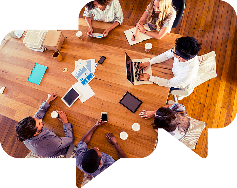 Aerial view of designers and engineers during a design meeting. The large wooden table around which they are seated contains sketches and notes as well as a series of laptops and mobile devices, such as tablets and smartphones.